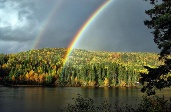 Regenbogen über einer natürlichen Landschaft aus Bergen, Wäldern und Seen